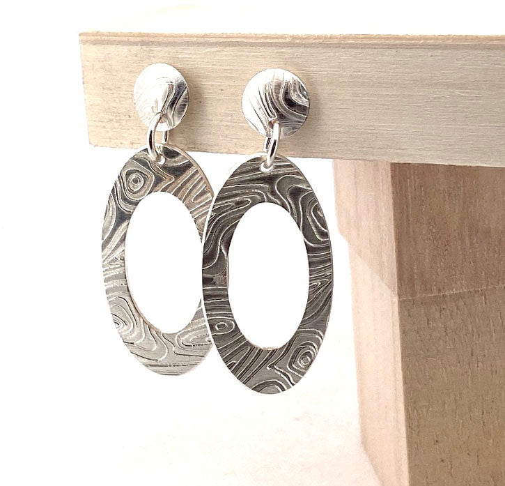 Engraved Oval earrings displayed upright on a wooden stand