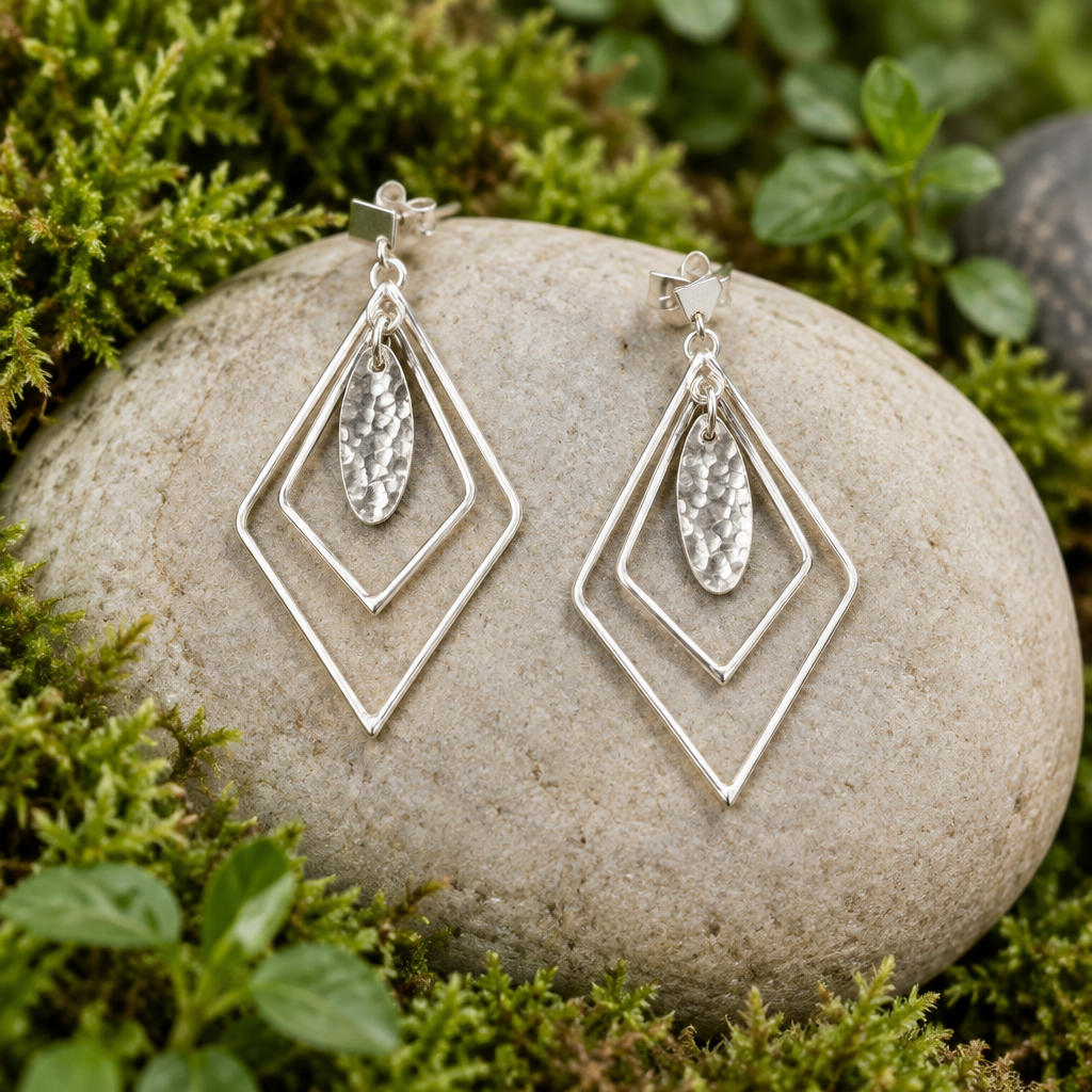 Prism sterling silver earrings on linen, showing nested diamond-shaped frames and hammered oval drops