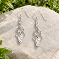 Lyra sterling silver drop earrings on a pebble, showing textured ovals and geometric frames