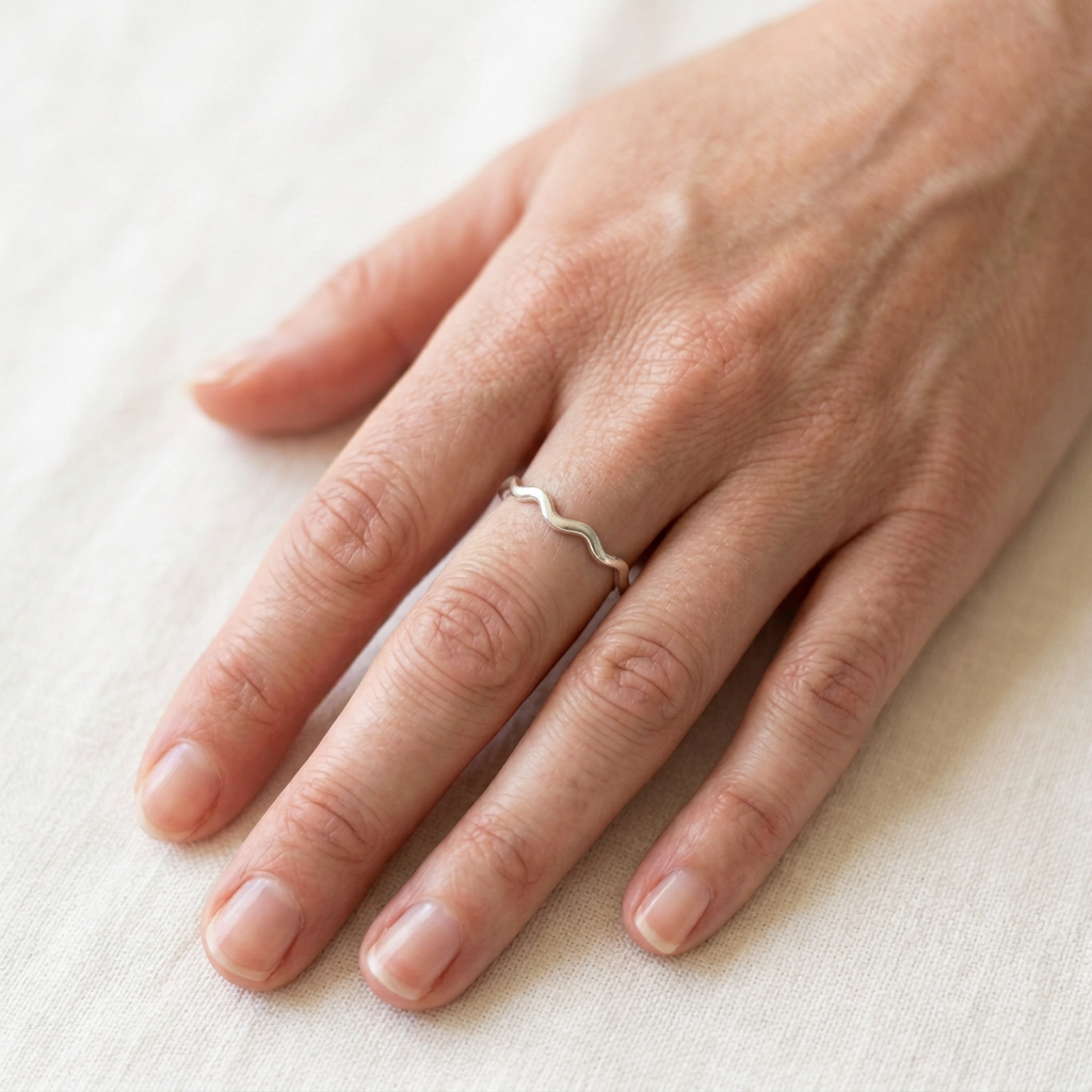 Fine wavy silver ring on a slender hand resting flat
