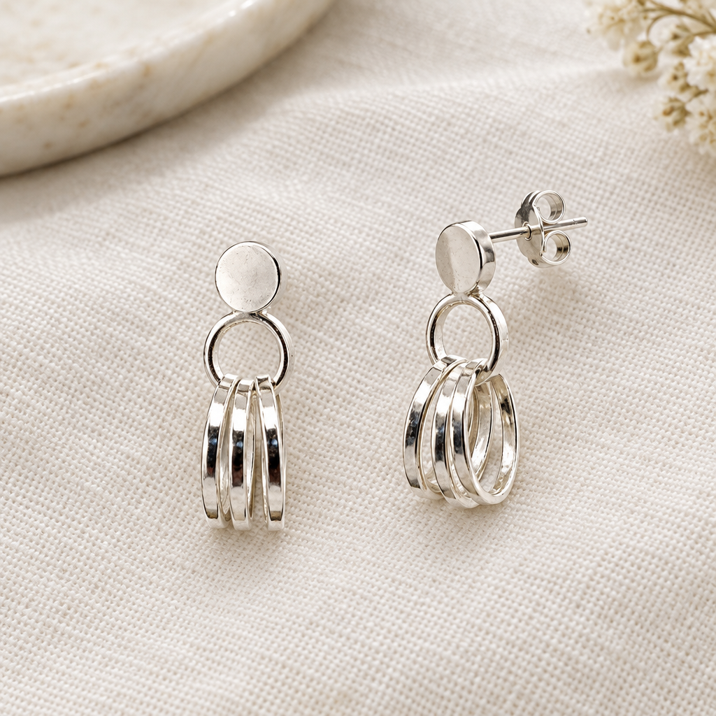 Pair of silver triple-hoop earrings laid on linen with a scroll back visible