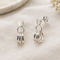 Pair of silver triple-hoop earrings laid on linen with a scroll back visible