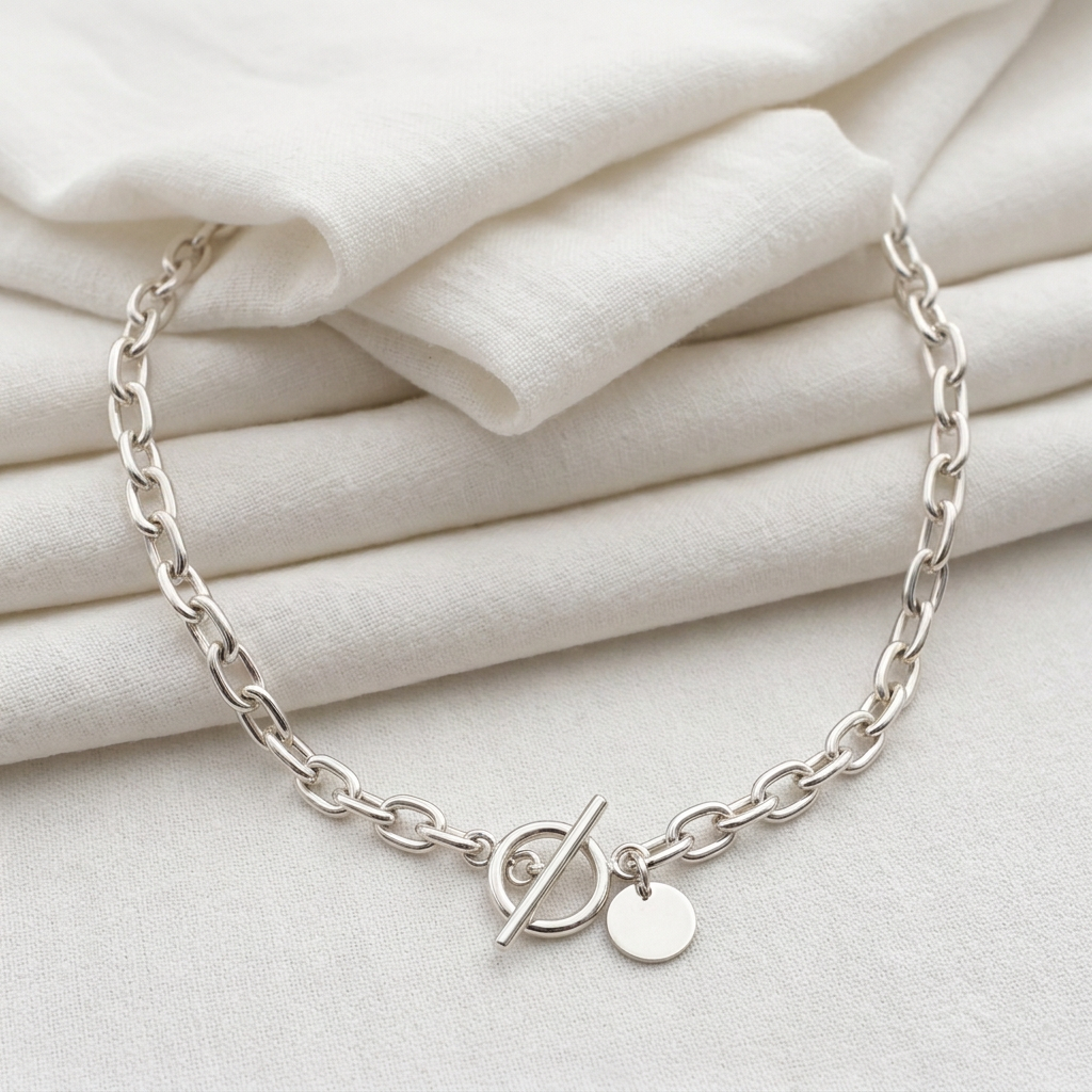 Silver anchor chain necklace partly concealed behind soft white fabric folds