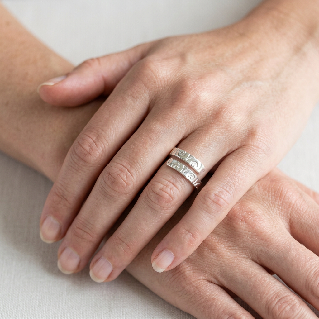 Spiral-patterned adjustable silver ring on slender hands in a relaxed wrist-crossing pose